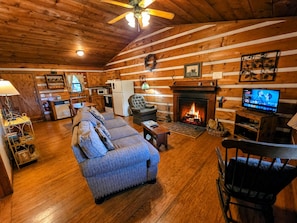 A cozy cabin interior with a fireplace, a sofa, a television, and a kitchen area.