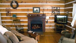 A cozy cabin interior with a fireplace, wooden walls, a television, and a sofa. - B's Nest a Private & Clean w Mtn Views & Hot Tubs! (Sevierville)
