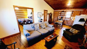 A cozy living room with a sofa, a wooden coffee table, and a dining area with a table and chairs. - B's Nest a Private & Clean w Mtn Views & Hot Tubs! (Sevierville)