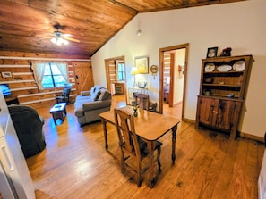 A cozy cabin interior with a wooden ceiling, a dining table with chairs, a sofa, and a bookshelf. - B's Nest a Private & Clean w Mtn Views & Hot Tubs! (Sevierville)