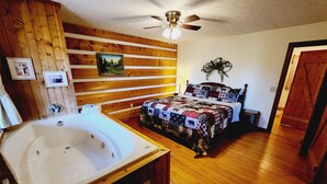 A wooden-paneled room with a large bathtub, a bed with a quilt, and a ceiling fan. - B's Nest a Private & Clean w Mtn Views & Hot Tubs! (Sevierville)