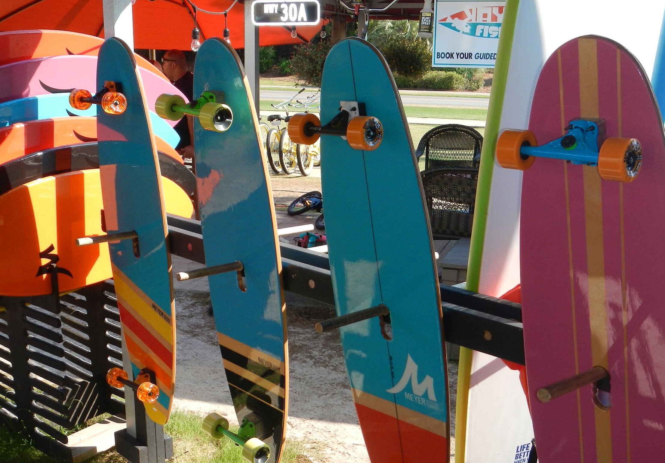 En rad färgglada skateboardar står utställda utomhus, och i bakgrunden syns en skylt.