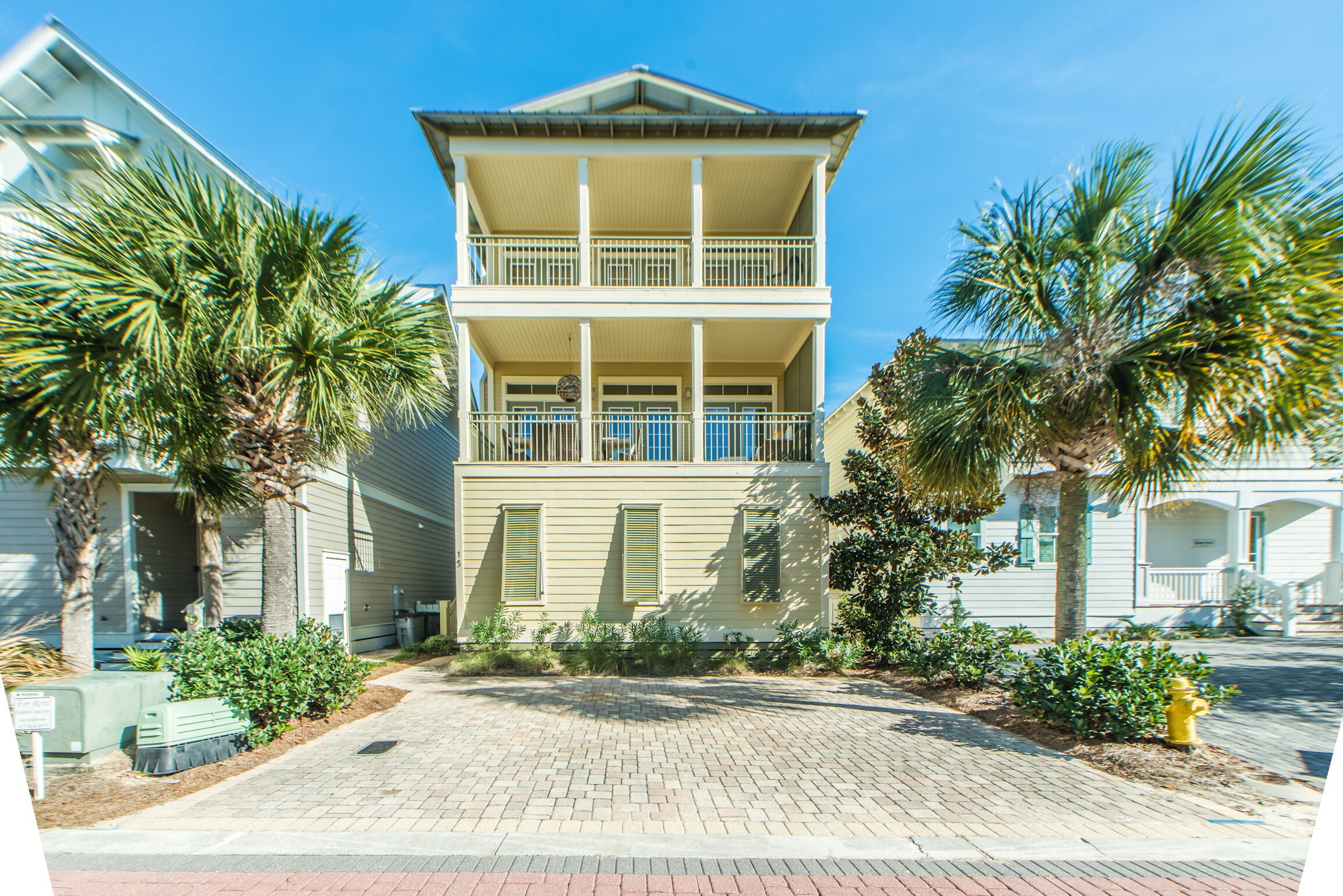 A two-story building with a balcony on the upper floor, surrounded by palm trees and a brick driveway.
