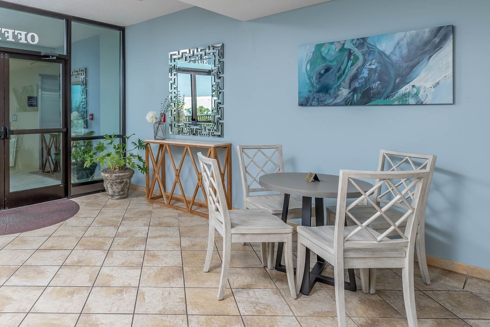 A dining area with a round table and four chairs, a decorative mirror, and a painting on the wall.