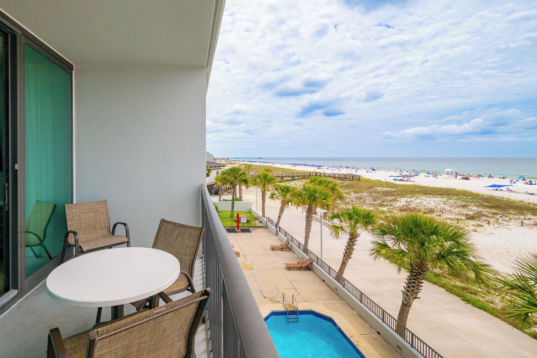 A balcony with wicker chairs, a small pool, and a view of the beach.