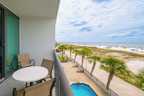 A balcony with wicker chairs, a small pool, and a view of the beach.