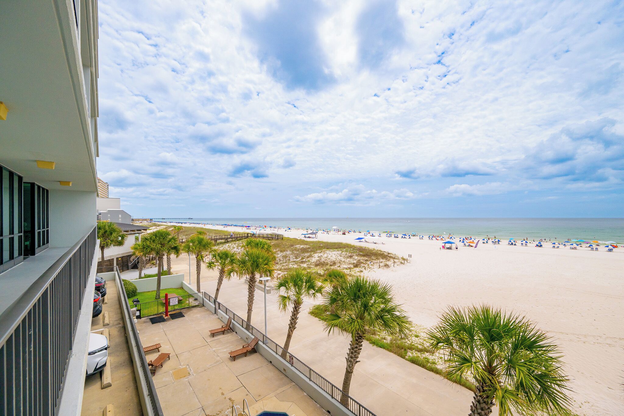 A beach view from a balcony with palm trees, a sandy beach, and umbrellas.