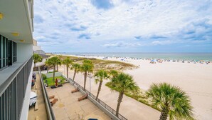 A beach view from a balcony with palm trees, a sandy beach, and umbrellas. - *Roll-in Shower* Wheelchair Accessible Beach Front Hotel Suite (Gulf Shores)