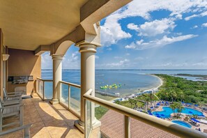 A balcony with a view of a beach, a pool, and a dock with boats.