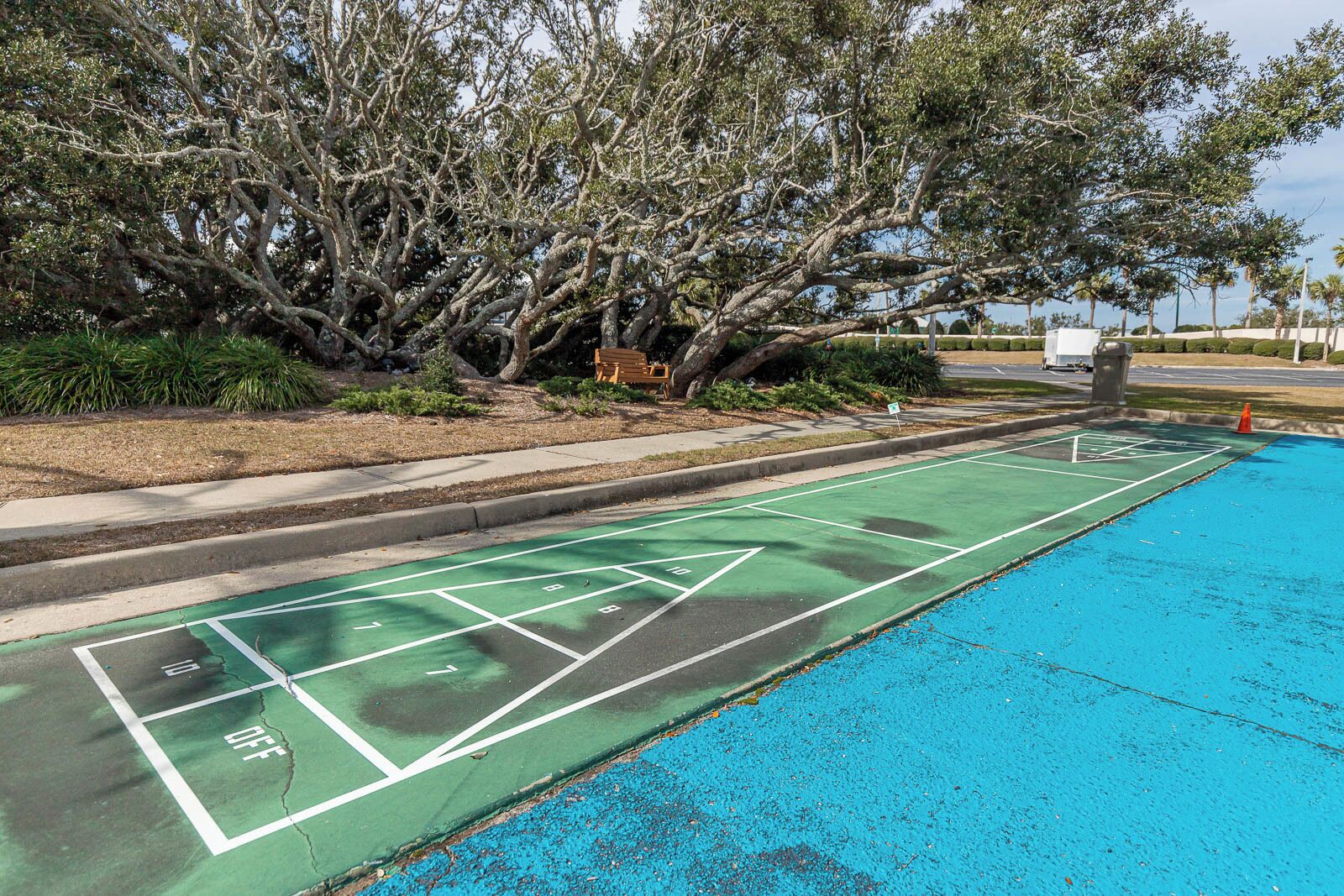 A shuffleboard court adjacent to a pool with a tree-lined background.