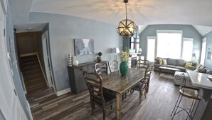 A spacious dining area with a wooden table and chairs, a chandelier, and a view of the living room with a sofa and a staircase leading to another room. - Short walk to the village-Stunning upgraded Rivergrass condo w/ beautiful decor (The Blue Mountains)