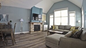 A spacious living room with a stone fireplace, a grey sofa, and a dining area with wooden chairs. - Short walk to the village-Stunning upgraded Rivergrass condo w/ beautiful decor (The Blue Mountains)
