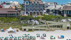 Un hotel frente al mar con una torre destacada, un paseo marítimo y sombrillas de playa.