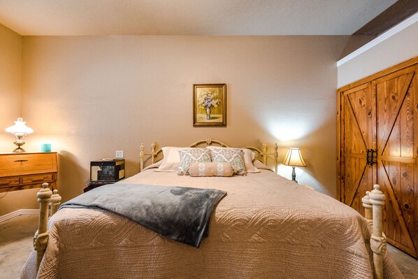A bedroom with a bed, a wooden wardrobe, a dresser, and a painting on the wall.