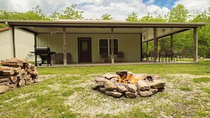 A covered outdoor area with a fire pit, a building with a door and windows, and a stack of firewood. - Hannah House ~ Your Vacation Awaits! (Huntsville)