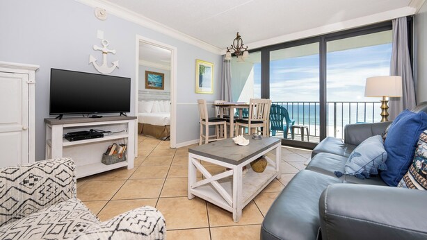 Una sala de estar moderna con un televisor de pantalla plana, una zona de comedor con sillas, un sofá y un balcón con vistas al mar.
