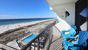 Un balcón con piscina, vista a la playa y sillas azules.
