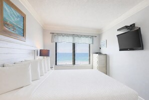 A bedroom with a bed, a TV, a window with a view of the sea, and a painting on the wall.