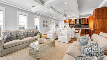 A spacious living room with a large sofa, a coffee table, and a kitchen area in the background.