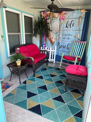 A cozy porch area with wicker furniture, a colorful rug, and a decorative backdrop with beach-themed decor.