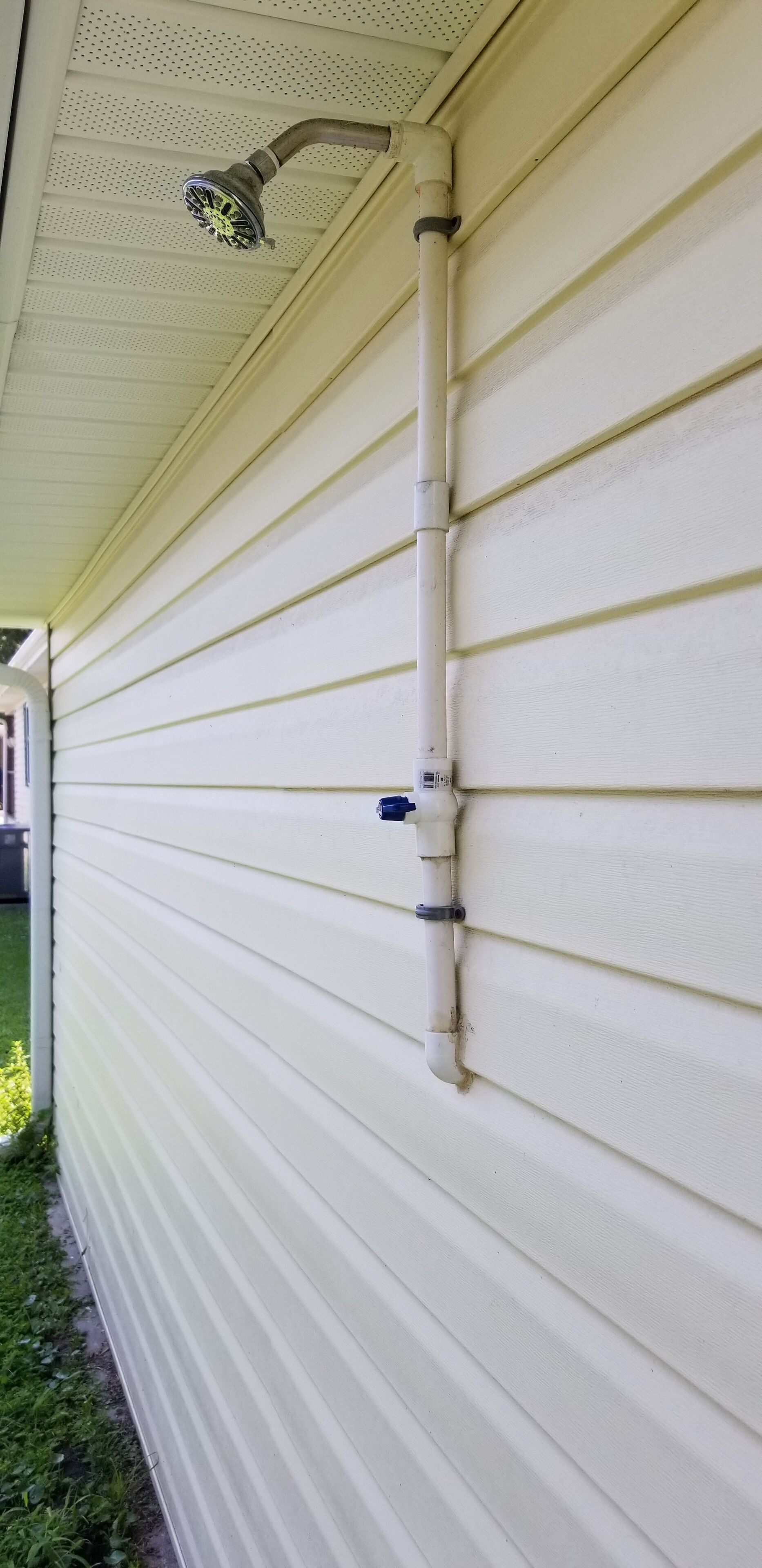 A white exterior wall with horizontal siding and a white downspout with a blue valve.
