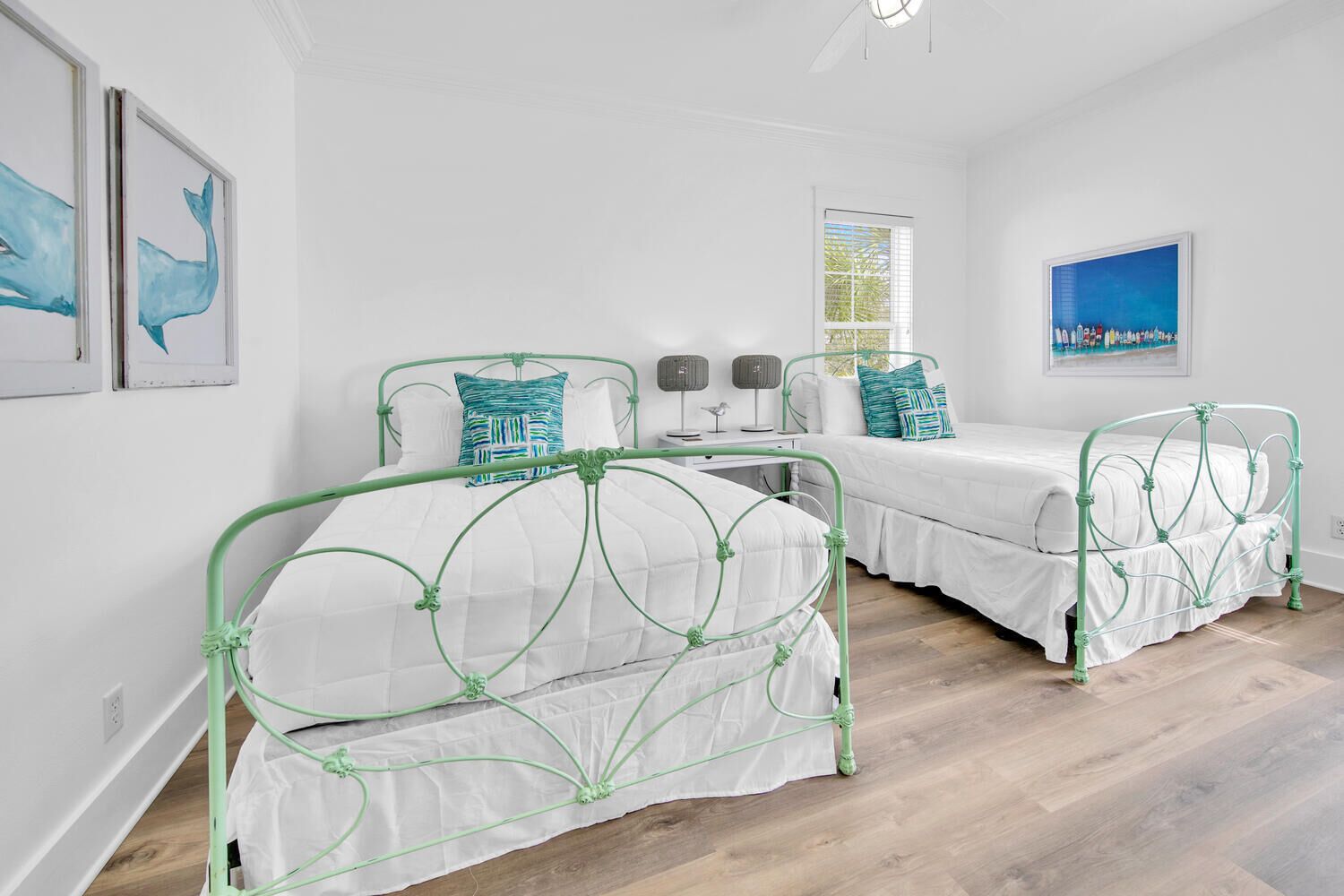 A bedroom with two green metal beds, white bedding, and a window with blinds.