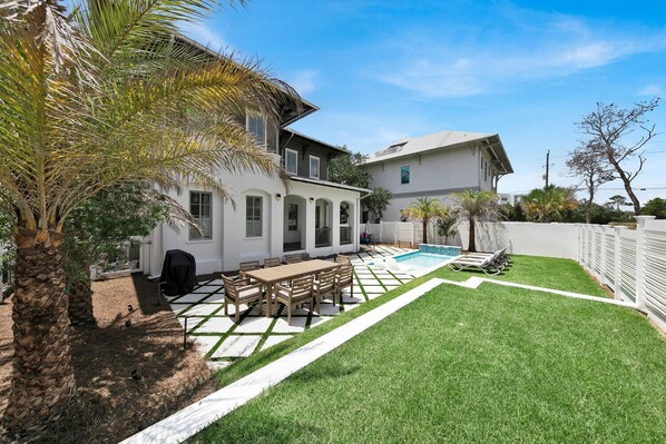 A backyard with a pool, a dining area, and a white fence.