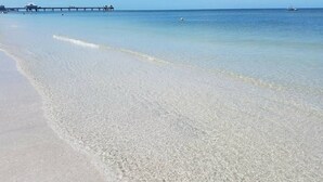 A beach with clear shallow water, a pier in the background, and a boat on the water. - Always Family First Water Front Condo ⭐️⭐️⭐️⭐️⭐️ (Clearwater)