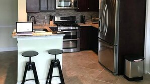 A modern kitchen with dark wood cabinets, stainless steel appliances, a central island with stools, and pendant lighting. - Always Family First Water Front Condo ⭐️⭐️⭐️⭐️⭐️ (Clearwater)