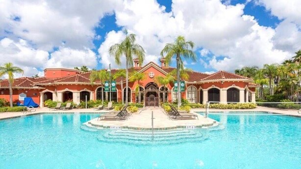 A pool area with a central fountain, surrounded by palm trees and a building with a red facade and arched windows. - Always Family First Water Front Condo ⭐️⭐️⭐️⭐️⭐️ (Clearwater)