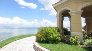 A covered outdoor area with a view of a bridge over water, surrounded by greenery and a paved walkway. - Always Family First Water Front Condo ⭐️⭐️⭐️⭐️⭐️ (Clearwater)