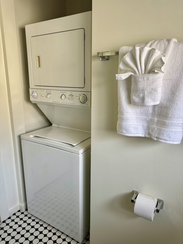 A compact laundry area with a washing machine, a drying rack, and a toilet paper holder.
