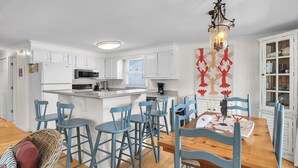 A modern kitchen with white cabinets, a central island, and blue chairs. - Sunkissed 2: Comfortable Cottage Near Public Beach Access (Oak Island)