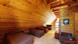 Une cabane en rondins avec un plafond incliné, des murs en bois et un intérieur chaleureux, comprenant un canapé et un téléviseur.