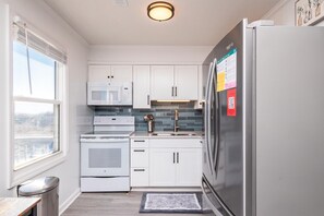 A modern kitchen with white cabinets, stainless steel appliances, and a window providing a view.