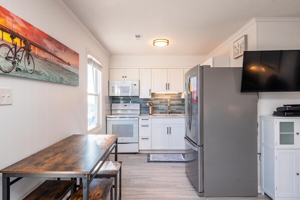 Enjoy cooking in this kitchen with a gas stove, microwave, and refrigerator, complemented by a dining table and bench.