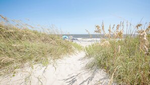 A sandy path leading to a beach with a clear sky.