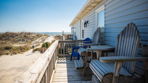 A wooden deck with a view of the beach, a table, and two chairs.