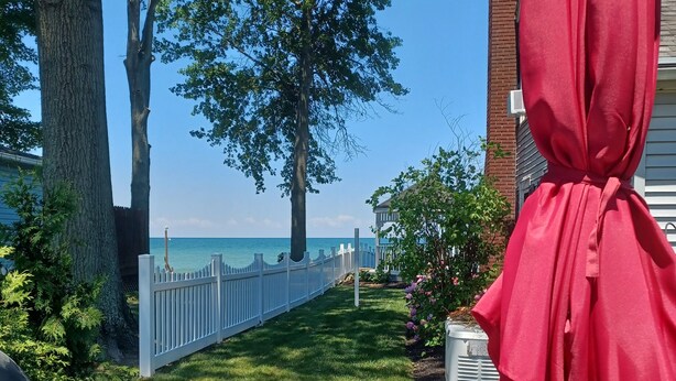 A patio area with a glass table, striped lounge chair, and a red umbrella. - Lake Erie Cottage w/ Private Beach Access - Couples Retreat (Madison)