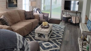 A cozy living room with a sofa, coffee table, and TV. - Lake Erie Cottage w/ Private Beach Access - Couples Retreat (Madison)