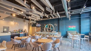A modern cafe with round tables and chairs, a bar area, and a neon sign. - Aloft by Marriott Buffalo Downtown (Buffalo)