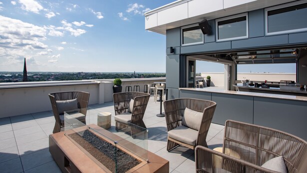 A rooftop terrace with wicker furniture, a bar area, and a view of the cityscape. - Aloft by Marriott Buffalo Downtown (Buffalo)