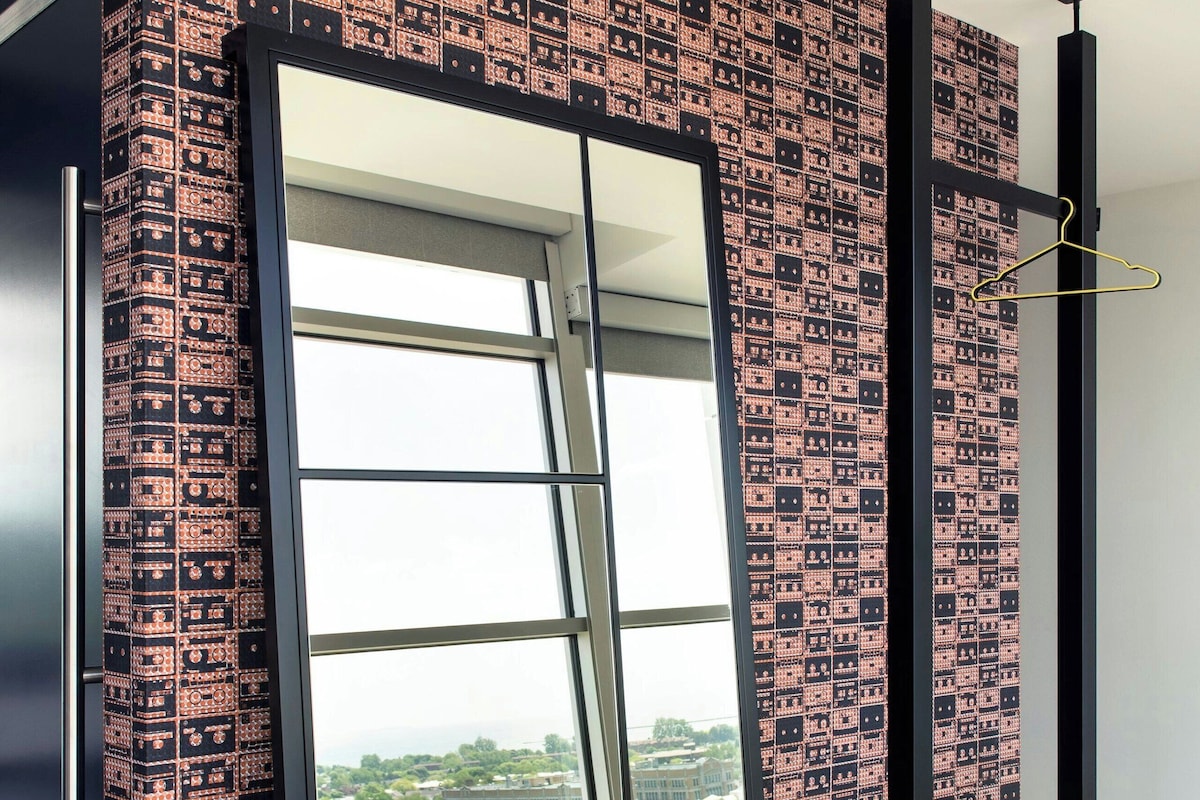Una habitación con un espejo grande, papel tapiz estampado, un aparador de madera y vistas a la ciudad.