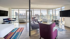A modern living room with a large window, a flat-screen TV, a sofa, a coffee table, and a patterned rug. - Aloft by Marriott Buffalo Downtown (Buffalo)