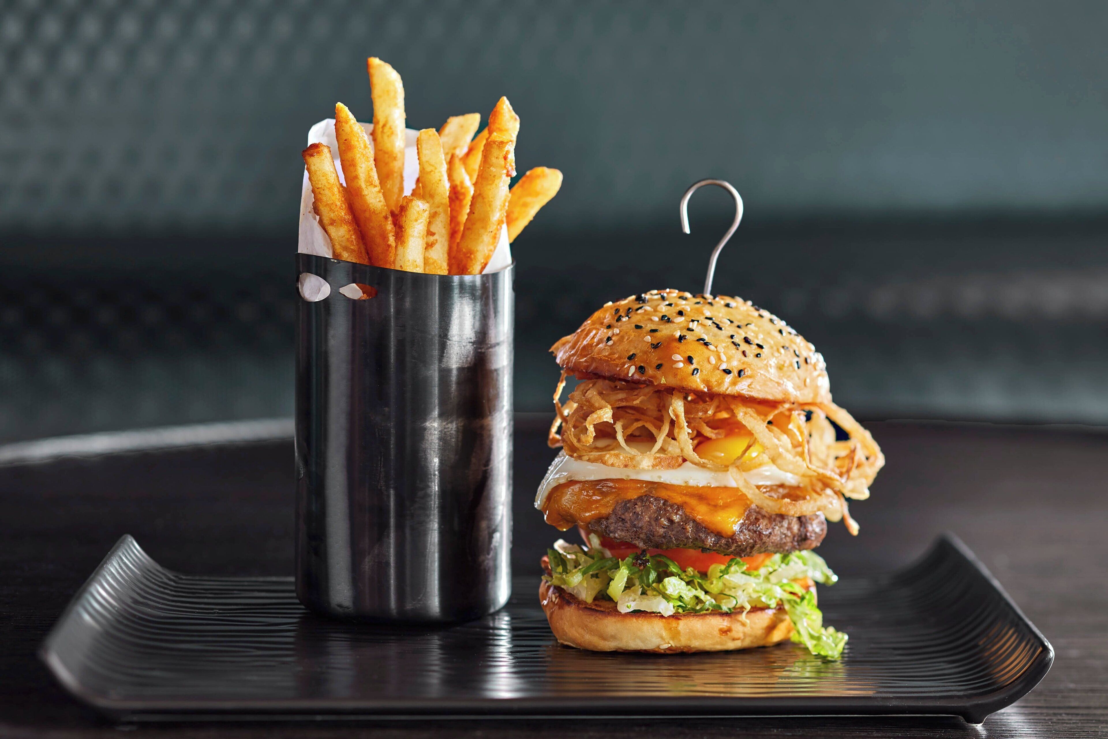 Un hamburger servi dans un pain aux graines de sésame, avec de la laitue, des tomates et du fromage, accompagné d’une portion de frites.