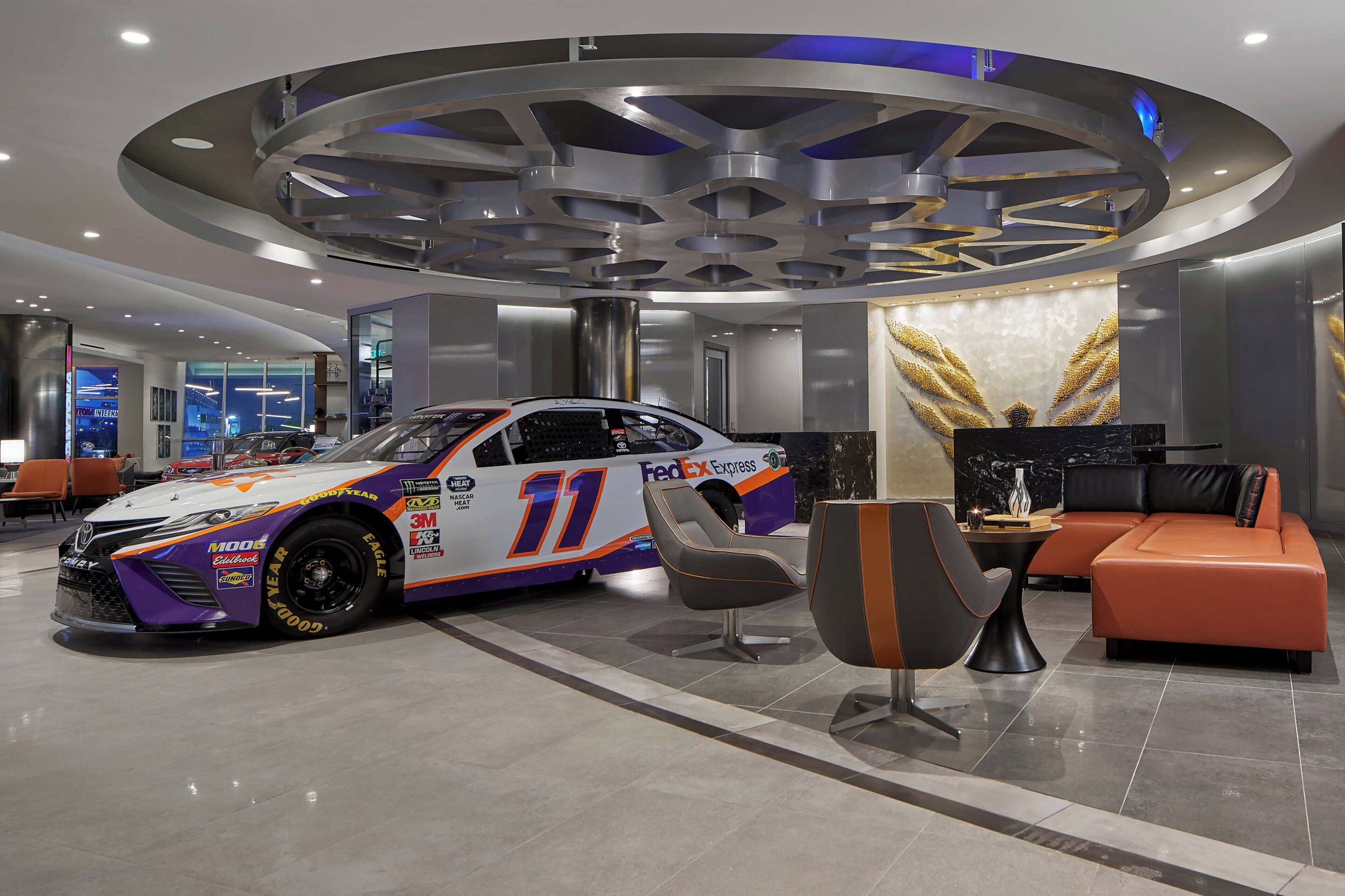Eine moderne Hotelhalle mit Rennauto, Sitzgelegenheiten und einem großen, runden Deckenleuchten-Design.