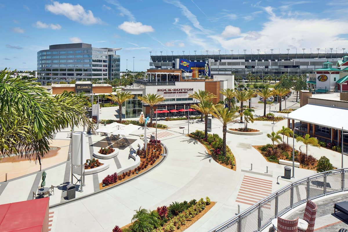 A modern hotel with a central courtyard, outdoor seating, and a view of a stadium in the background.