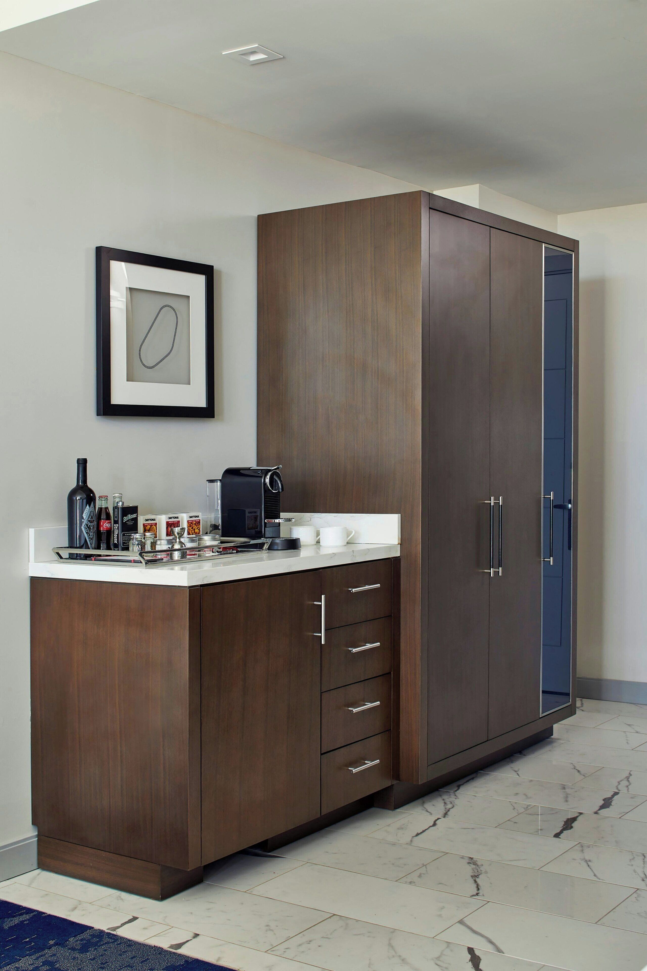 A modern kitchen with a dark wood cabinet, a coffee machine, and a framed picture on the wall.