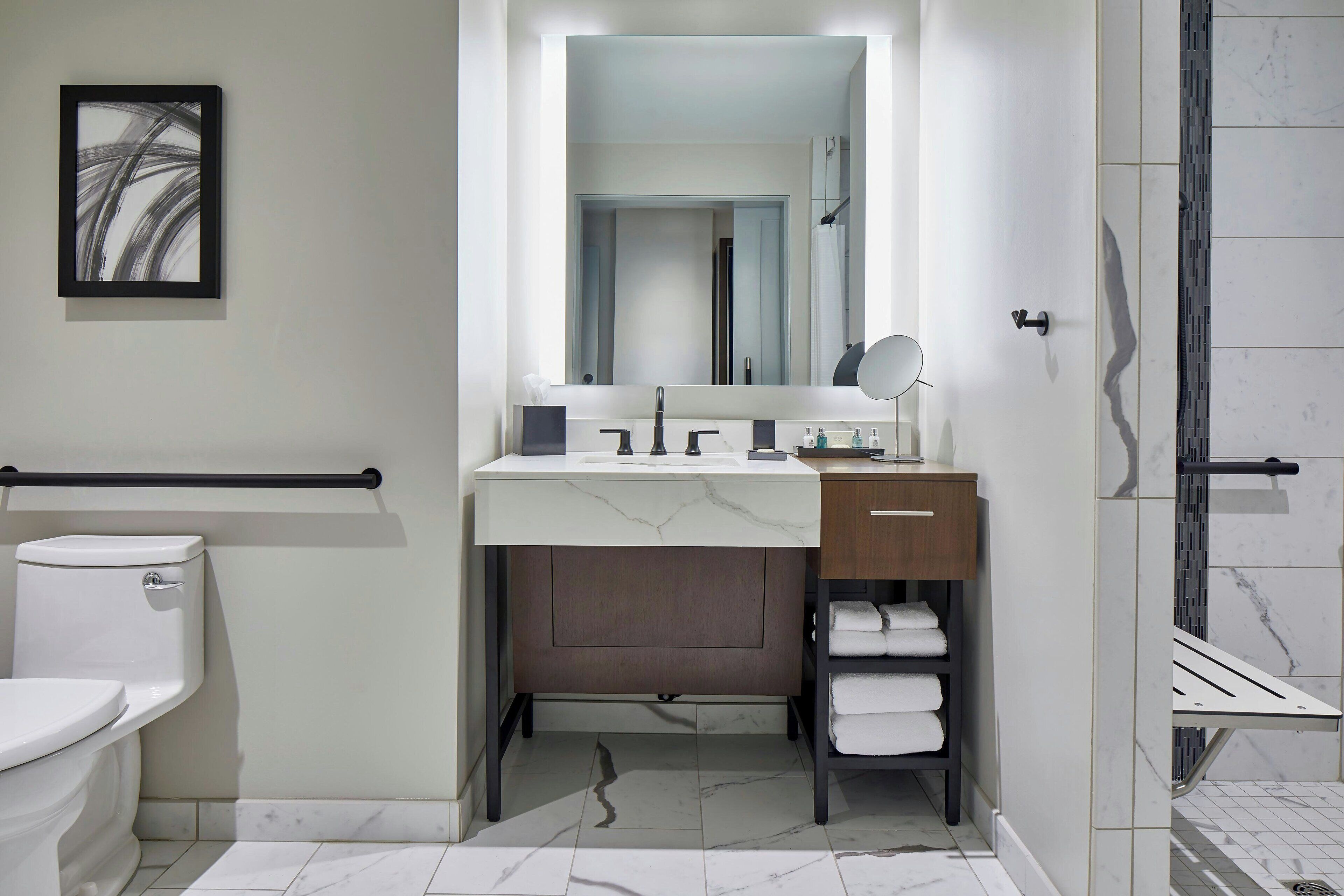 A modern bathroom with a toilet, sink, mirror, and shower area.