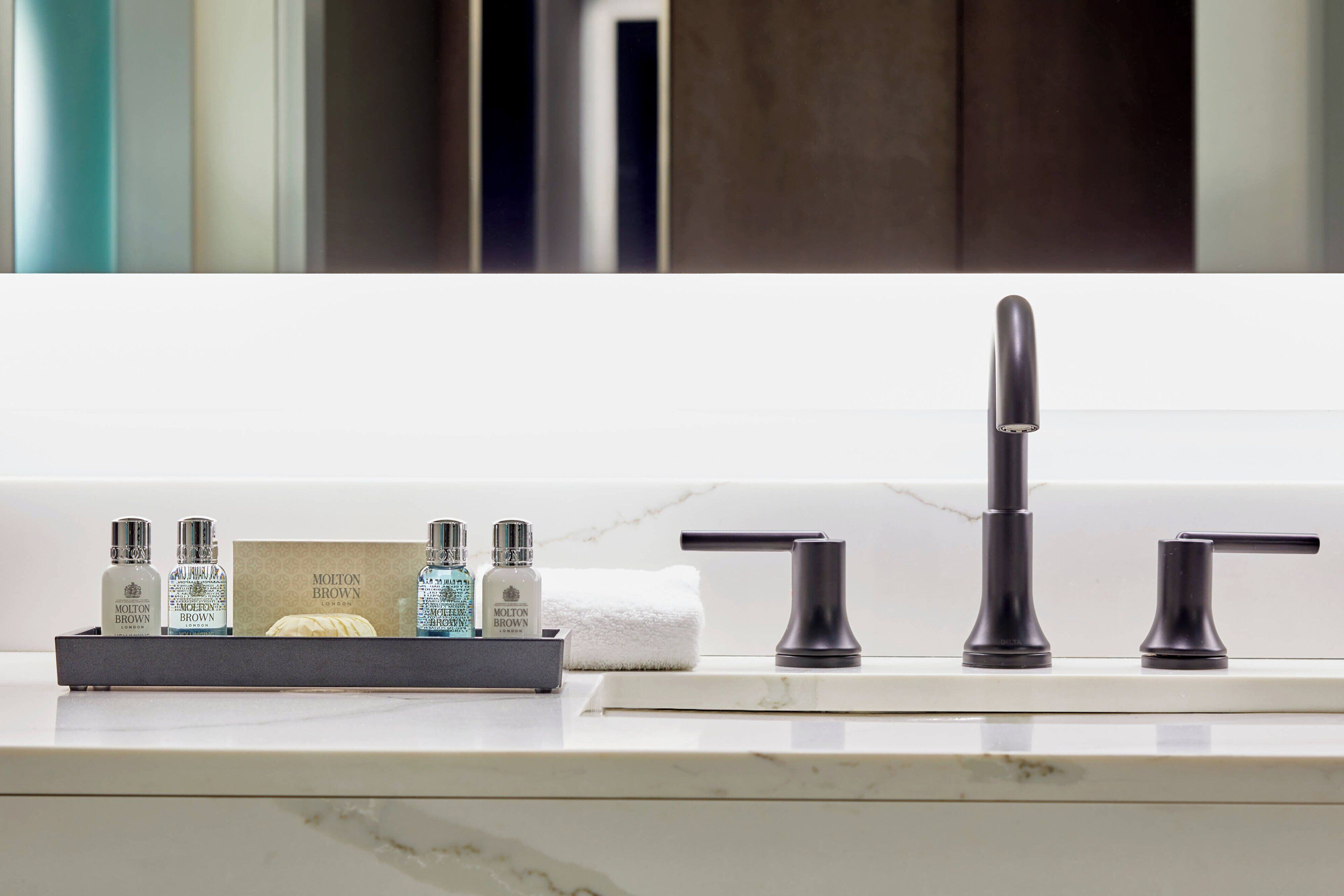 A bathroom with a modern sink, two faucets, and a tray holding toiletries including bottles and a card.